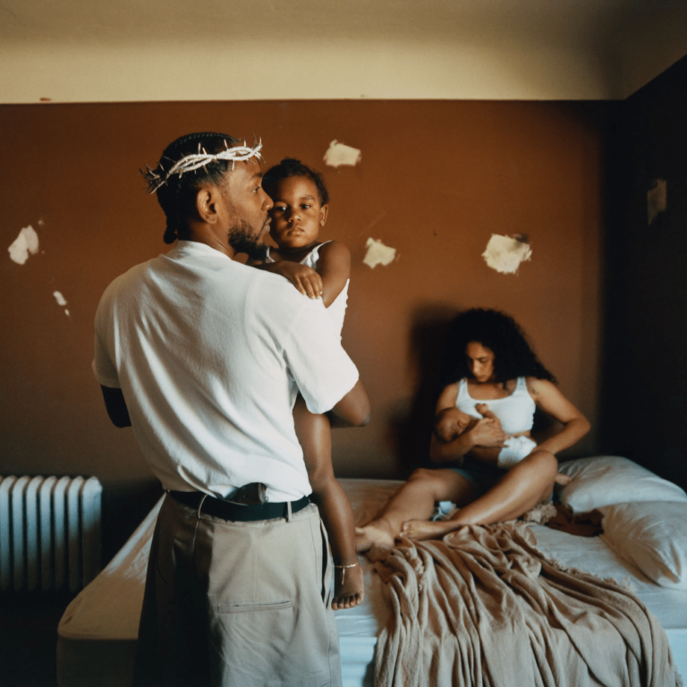 Ein Mann mit Dornenkrone hält sein Kind im Arm, während eine Frau auf dem Bett sitzt – intime Szene einer jungen Familie in schlichtem Raum, inspiriert vom Artwork zu „Mr. Morale & The Big Steppers“ von Kendrick Lamar.