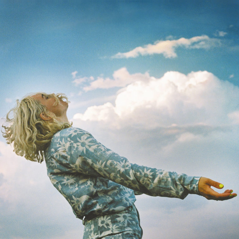 „HAAi steht vor einem weiten Himmel mit Wolken, die Ruhe und Weite symbolisieren, passend zu ihrer musikalischen Mischung aus Techno und natürlicher Klangwelt.“