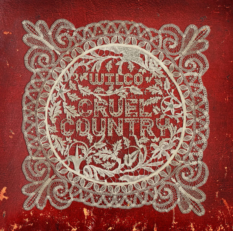 Das Albumcover „Cruel Country“ von Wilco zeigt ein rotes Bandana mit einem weißen Paisley-Muster, in dessen Mitte der Albumtitel steht, auf einem braunen, leicht abgenutzten Hintergrund.