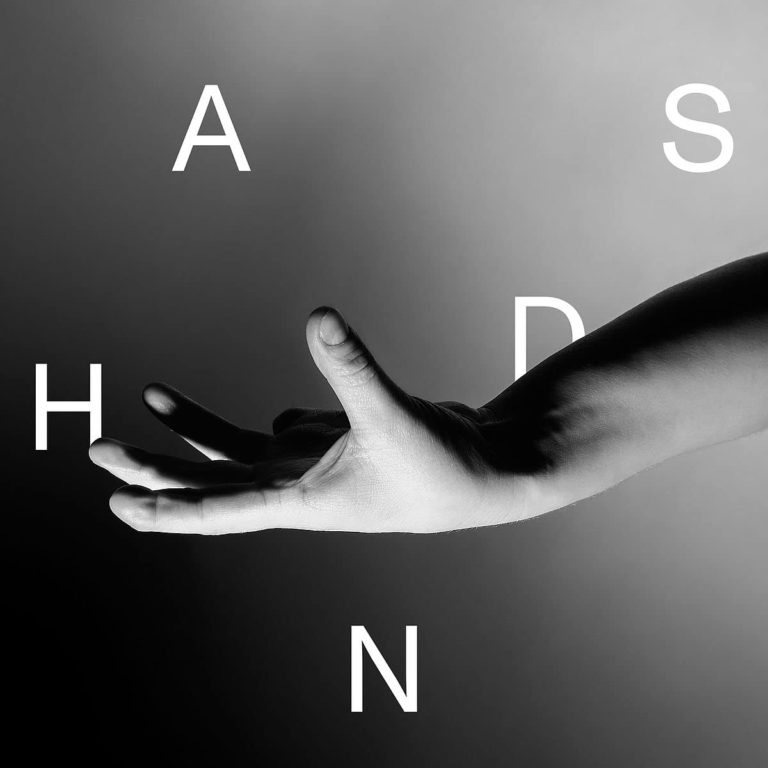 Schwarz-weißes Albumcover von „HANDS“ von Wallis Bird zeigt einen ausgestreckten Arm mit offener Handfläche vor einem unscharfen, grauen Hintergrund. Große weiße Buchstaben schweben locker um die Hand.