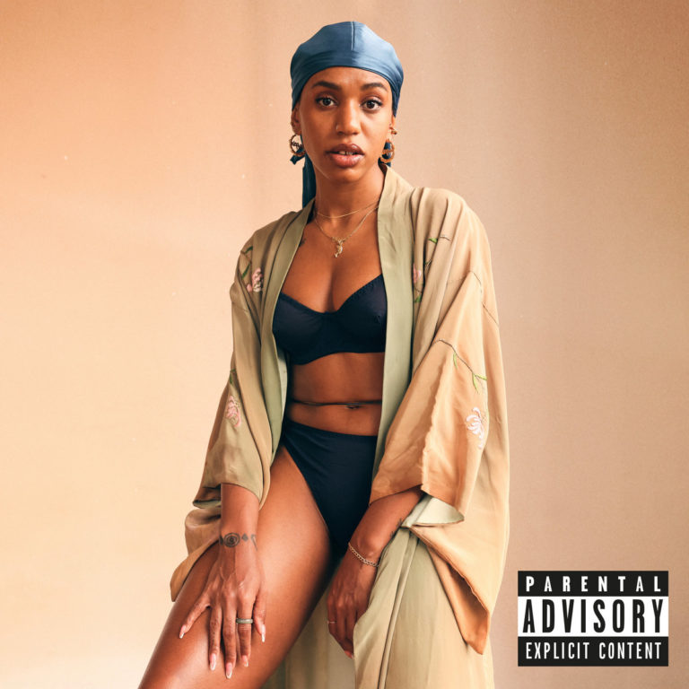 Albumcover von Remember Your North Star: Yaya Bey sitzt in schwarzer Unterwäsche und einem beigen Kimono vor pfirsichfarbenem Hintergrund. Sie trägt goldene Creolen, eine Kette und ein himmelblaues Durag – ihr Blick ist direkt, selbstbewusst, sanft und unmissverständlich.