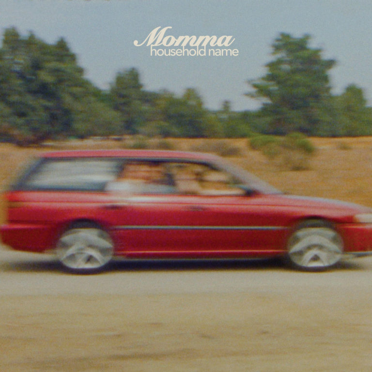 Cover des Albums „Household Name“ von Momma: Ein unscharf vorbeirasendes rotes Auto auf staubiger Landstraße, die Silhouetten zweier junger Menschen sichtbar – eingefangen im retrohaften 90s-Look. Oben mittig der weiße Albumtitel in nostalgischer Schrift.