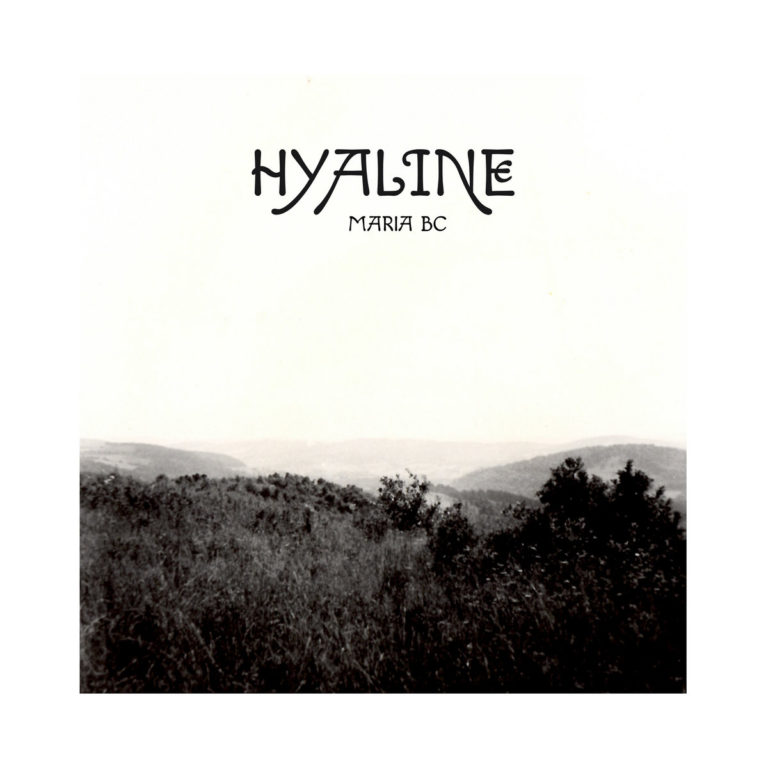 Das Cover zu „Hyaline“ von Maria BC zeigt eine körnige Schwarzweiß-Fotografie einer ruhigen, hügeligen Landschaft. Die Stimmung ist leer, entrückt und introspektiv – ein stilles Echo von Zeit, Raum und Erinnerung.