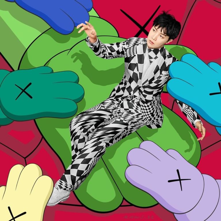 Der Künstler j-hope liegt im Schachbrettanzug auf einem poppigen, surrealen Hintergrund aus cartoonartigen, bunten Händen – verspielt, rebellisch, symbolisch.