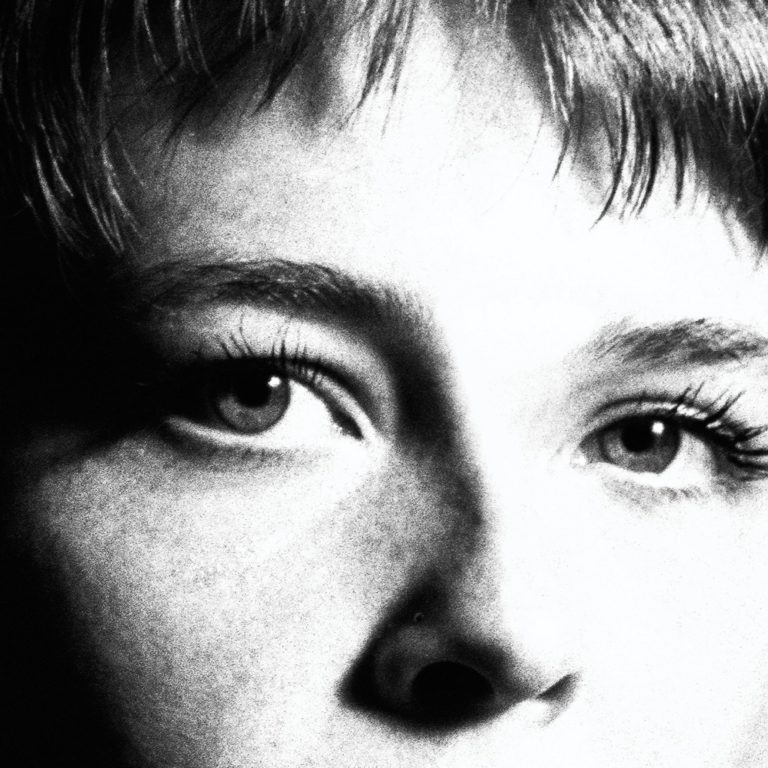 Nahaufnahme von Maggie Rogers’ Gesicht in grobkörnigem Schwarz-Weiß – eindringlicher Blick, kurze Haare, starkes Licht-Schatten-Spiel als Symbol für das Album „Surrender“.