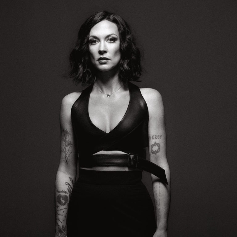 Amanda Shires in Schwarz-Weiß-Porträt, mit kurzem dunklen Haar, Blick in die Kamera, sichtbaren Tattoos und einem selbstbewussten, ungeschönten Ausdruck.