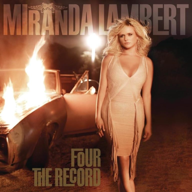 Miranda Lambert steht vor einem brennenden Auto in einem beigefarbenen Kleid.