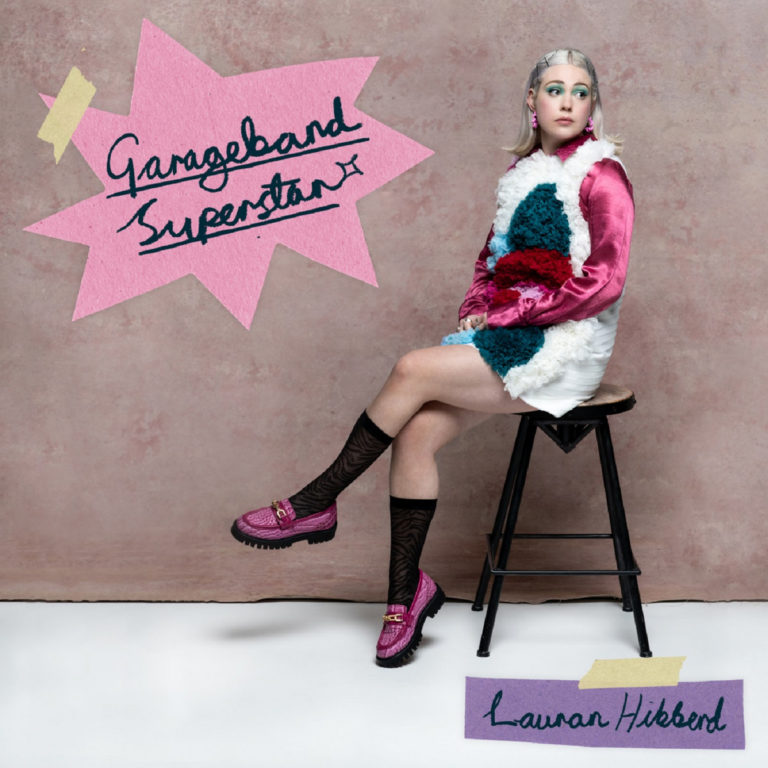 Vor rosa strukturiertem Hintergrund sitzt Lauran Hibberd in einem auffälligen Retro-Outfit auf einem Hocker. Sie blickt selbstbewusst zur Seite, während handschriftliche Textelemente wie „Garageband Superstar“ auf pinkem Papier und ihr Name auf lila Tape montiert sind. Die Inszenierung wirkt wie ein schrilles Teen-Magazin-Cover aus den 2000ern – verspielt, stilisiert, ironisch.
