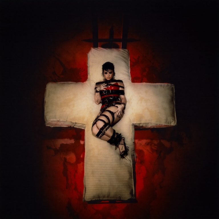 Demi Lovato liegt gefesselt in schwarzem Bondage-Outfit auf einem riesigen Kreuz aus Matratzen, das leuchtend vor einem blutroten Hintergrund schwebt. Die Szenerie wirkt sakral und provokant zugleich – eine visuelle Allegorie auf Opfer, Erlösung und mediale Kreuzigung. Ausdruck von Härte, Kontrollverlust und Selbstermächtigung.