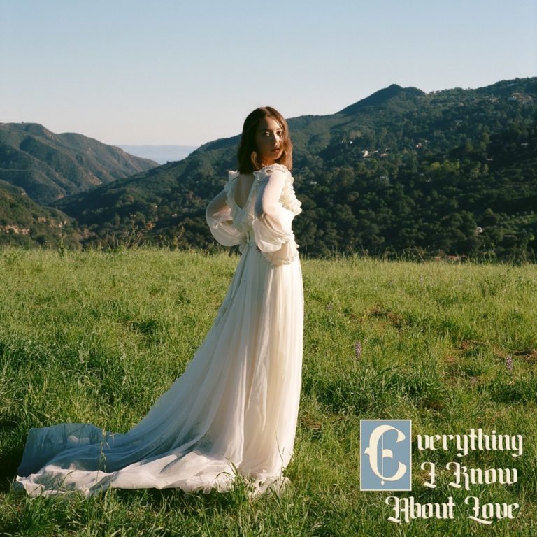 Cover des Albums „Everything I Know About Love“ von Laufey: Die Sängerin in einem weißen Kleid steht auf einer Wiese mit Bergpanorama im Hintergrund.