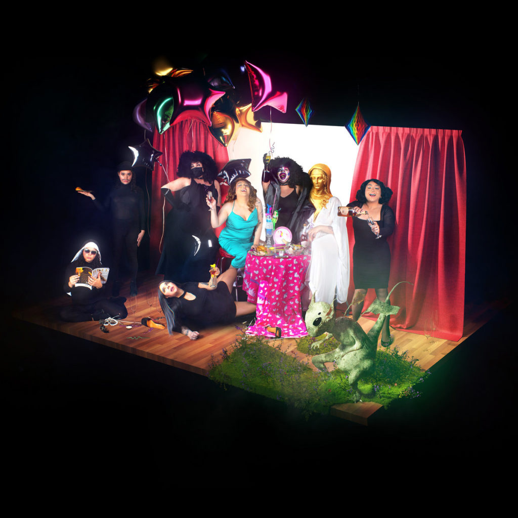 Eine vielfältige, bunte Truppe performt auf einer kleinen Bühne, zwischen Ballons, Vorhängen und skurrilen Details – ein Theaterstück der Identitäten und Befreiungen.