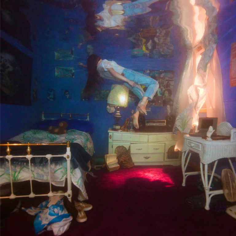 Person schwebt in einem blau beleuchteten, überfluteten Schlafzimmer mit Bett und Schreibtisch.
