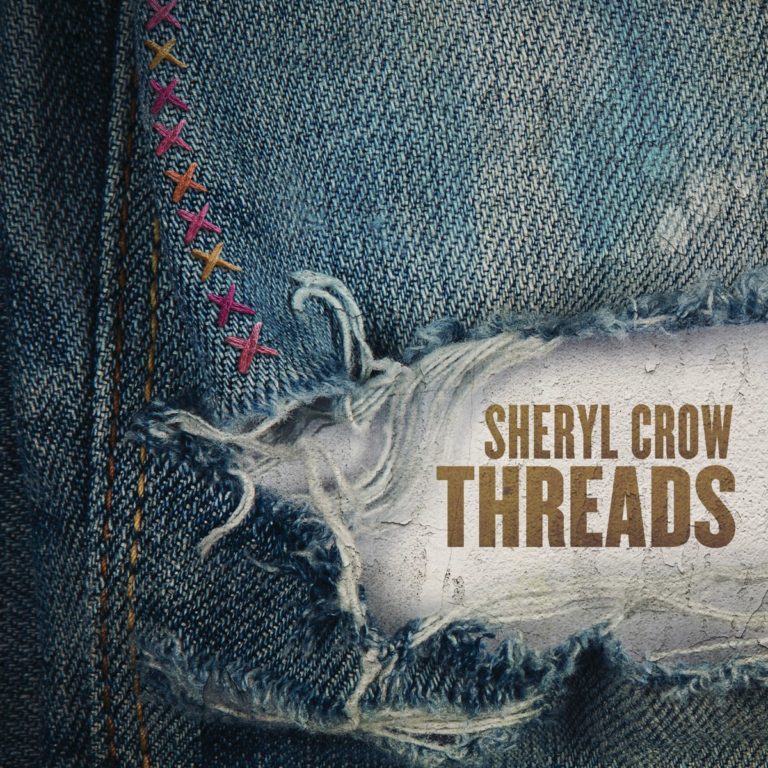 Nahaufnahme eines zerrissenen Jeansstoffs mit bunten Nähten und dem Albumtitel Sheryl Crow Threads.