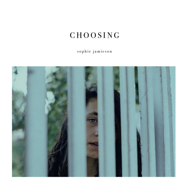 Auf dem Cover von Choosing blickt Sophie Jamieson hinter Gitterstäben hervor – ein intimes, zurückhaltendes Porträt, das Isolation, Verletzlichkeit und inneren Wandel visuell einfängt.