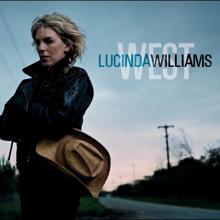Lucinda Williams steht mit einem Cowboyhut in der Hand an einer Straße, umgeben von einer melancholischen Landschaft.
