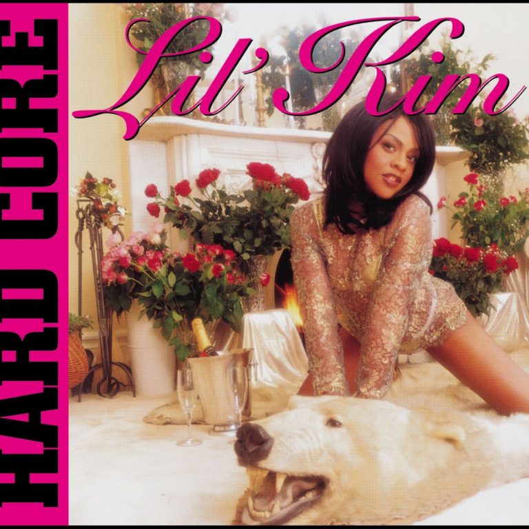 Albumcover von Hard Core von Lil’ Kim: Die Künstlerin kniet in durchsichtiger Spitzenwäsche auf einem Eisbärenfell vor einem Kamin, umgeben von Rosen und Champagnerflaschen.