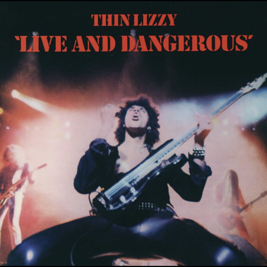 Live-Foto von Thin Lizzy’s „Live and Dangerous“-Cover: Frontmann Phil Lynott in ikonischer Pose mit Bass, rockend im Bühnenlicht der 70er.