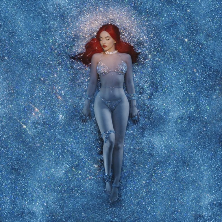 Ava Max liegt in glitzerndem blauen Funkeln, mit rotem Haar und funkelndem Outfit – Cover von „Diamonds & Dancefloors“, glamourös und traumhaft inszeniert.