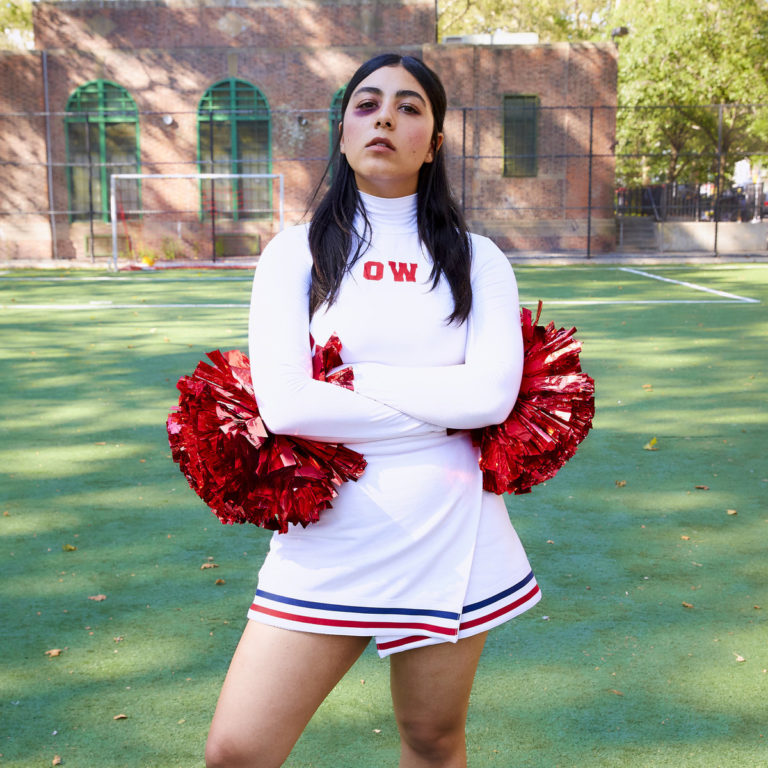 Person in Cheerleader-Outfit mit roten Pompons auf einem Sportplatz