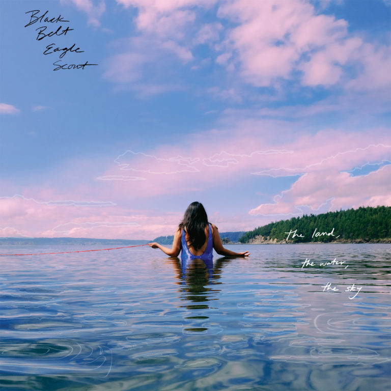 Cover von „The Land, The Water, The Sky“ von Black Belt Eagle Scout: Eine Person steht im klaren Wasser, blickt in den rosablauen Himmel, umgeben von Natur und Stille.