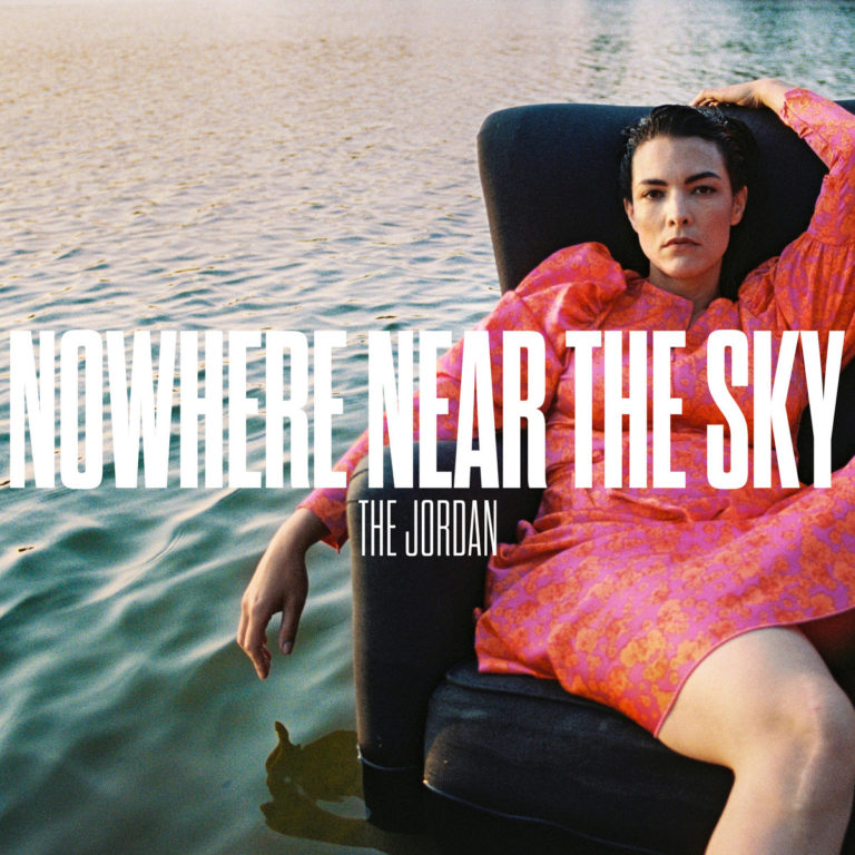 Cover von „Nowhere Near The Sky“ von The Jordan: Eine Frau in pinkem Kleid sitzt nachdenklich auf einem Sessel im Wasser, der Himmel spiegelt sich golden.