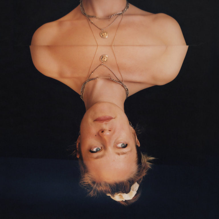 Albumcover von Anna B Savages „in|FLUX“ mit einem doppelt gespiegelt-gedrehten Porträt der Sängerin vor schwarzem Hintergrund, ruhig und intensiv zugleich.