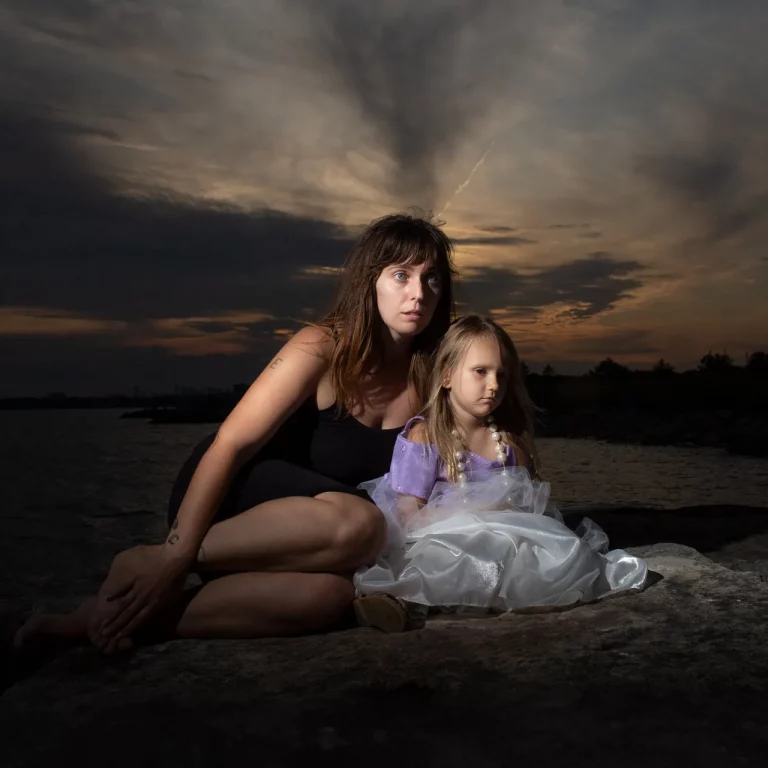 Frau und Kind sitzen bei Sonnenuntergang auf einem Felsen am Wasser.