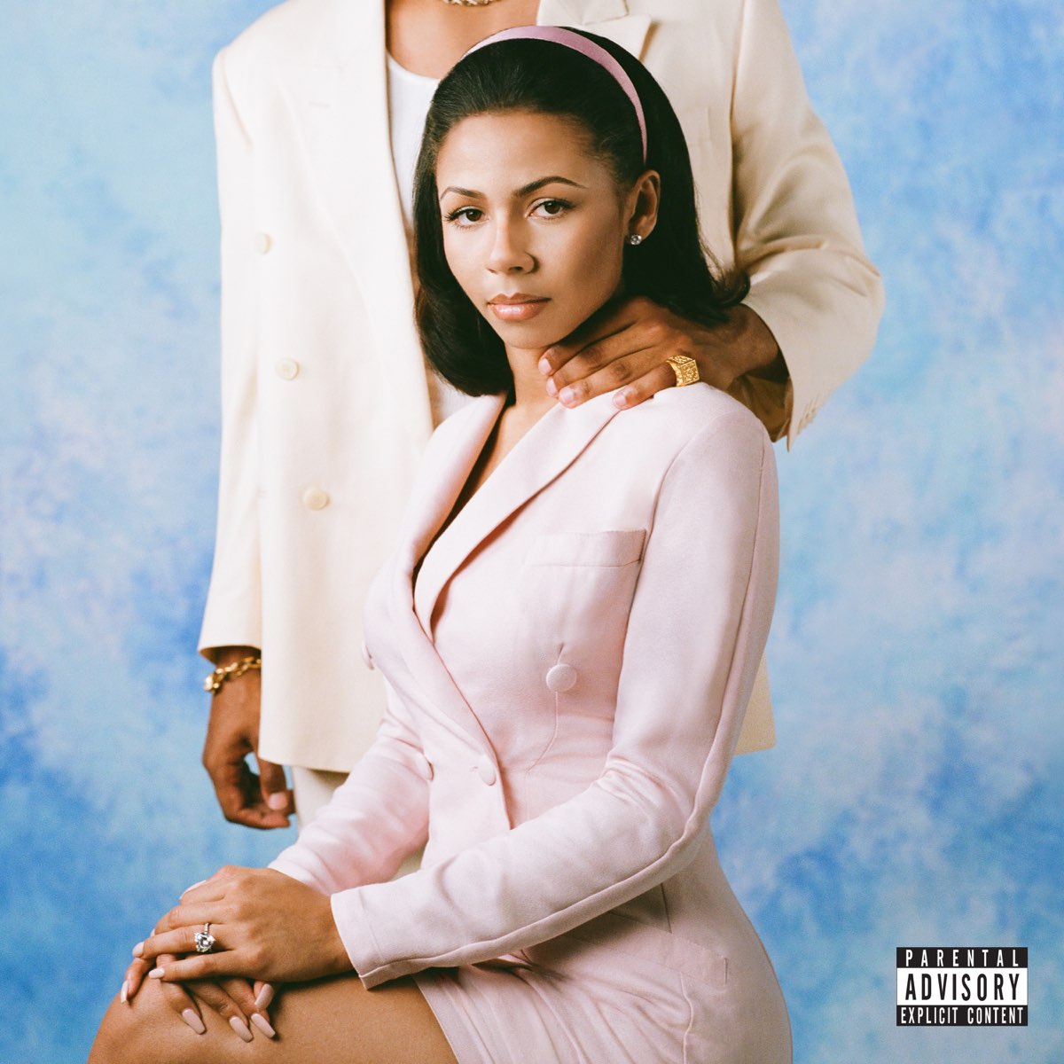 Frau in rosa Blazer sitzt vor blauem Hintergrund, Hand eines Mannes auf ihrer Schulter