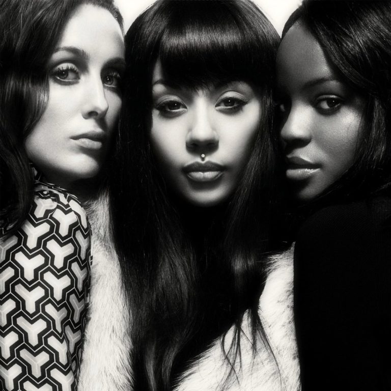 Mutya, Keisha und Siobhan in ikonischer Pose: Das Sugababes-Originaltrio blickt selbstbewusst und vereint in die Kamera – eine monochrome Hommage an britischen Pop mit Retro-Glamour und femininer Stärke.
