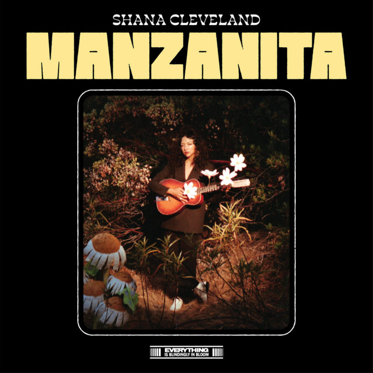 Cover des Albums „Manzanita“ von Shana Cleveland mit der Musikerin inmitten von Pflanzen, Gitarre in der Hand, vor dunklem Naturhintergrund – sanft beleuchtet.