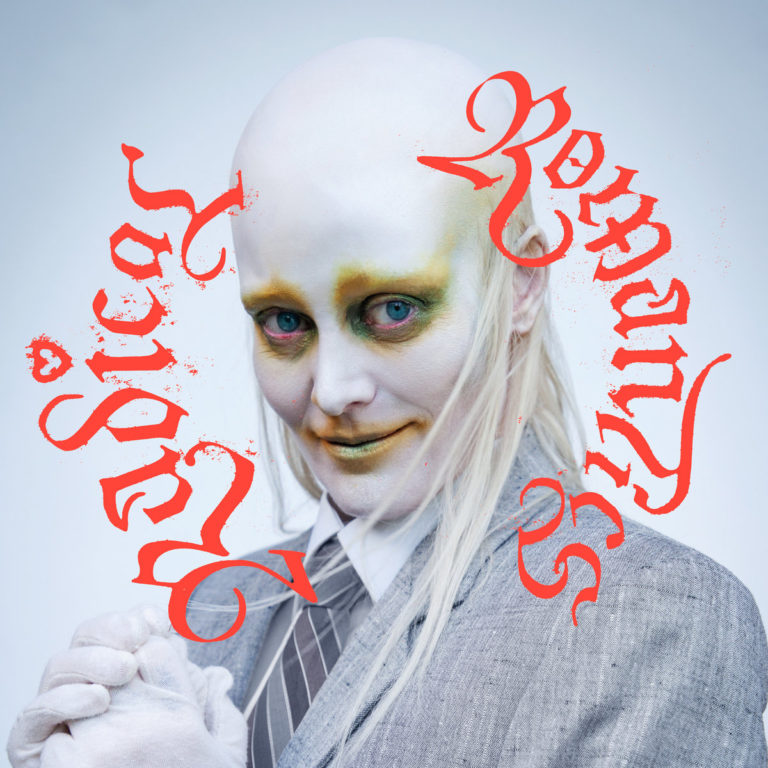 Cover des Albums „Radical Romantics“ von Fever Ray mit androgyn geschminktem Gesicht, stechend blauem Blick, grauem Anzug und rotem gotischem Schriftzug.