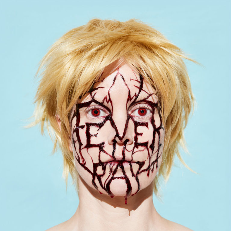 Gesicht mit blonden Haaren und roter Schrift auf hellem Hintergrund.