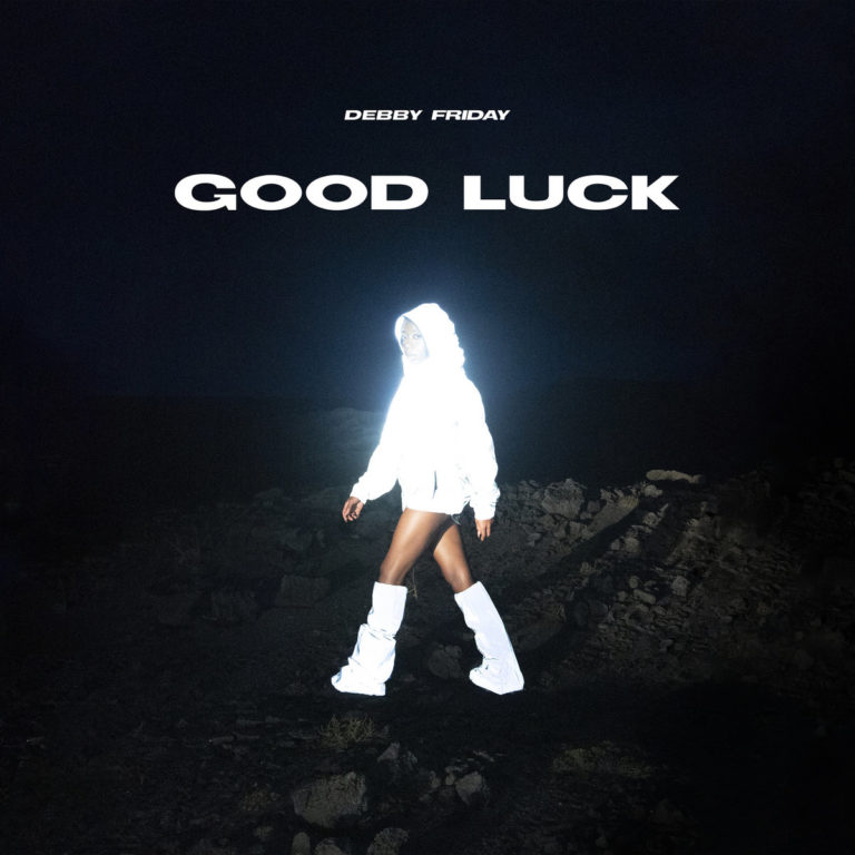Albumcover von „GOOD LUCK“ von Debby Friday: Eine Frau in reflektierend weißem Outfit schreitet durch dunkle, steinige Landschaft bei Nacht.