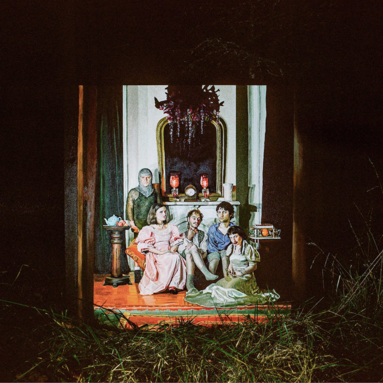 Albumcover von Wednesday – Rat Saw God: Szene im Stil eines Gemäldes, zeigt fünf Personen in altmodischer Kleidung vor einem Kamin, eingerahmt wie ein Theaterstück, mit surrealem Licht.