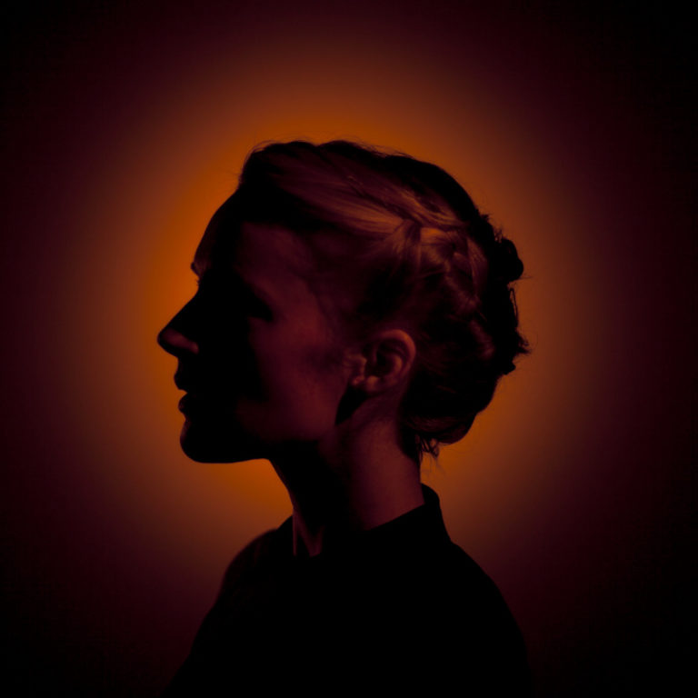 Silhouette einer Frau mit geflochtenem Haar vor orangefarbenem Hintergrund.
