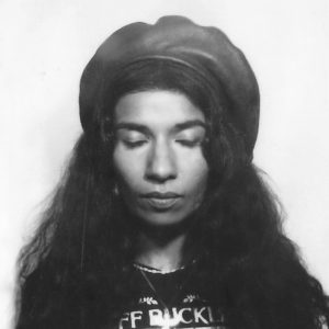 Schwarz-weiß Porträtfoto von Nabihah Iqbal mit geschlossenen Augen, Leder-Baskenmütze und langen Haaren; sie trägt ein Jeff Buckley Shirt.