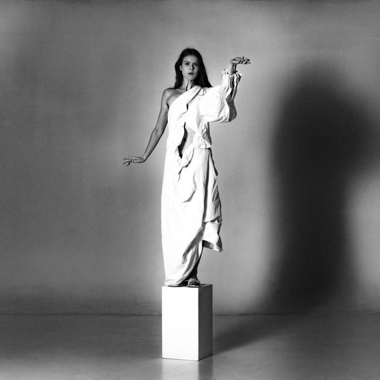 Albumcover zu „Museum“ von JFDR zeigt die Künstlerin in weißem Gewand, wie eine Skulptur auf einem Sockel stehend, in monochromer Studioaufnahme.