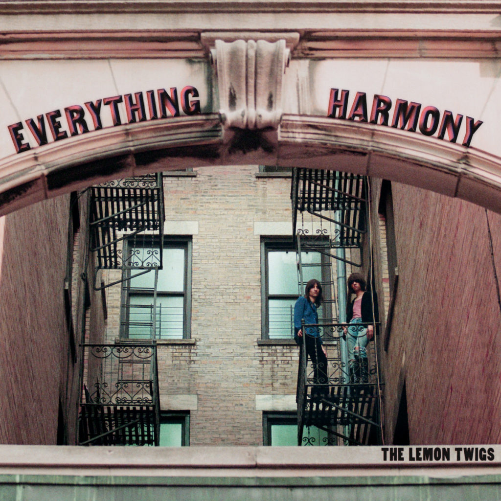 Zwei Bandmitglieder von The Lemon Twigs stehen auf einer Feuertreppe zwischen zwei Backsteingebäuden; über ihnen prangt der Albumtitel Everything Harmony in gebogenen Lettern.