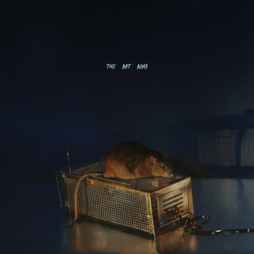 Albumcover zu „The Rat Road“ von SBTRKT zeigt eine braune Ratte auf einer Drahtfalle vor dunklem Hintergrund, mit Titeltext in Handschriftstil.