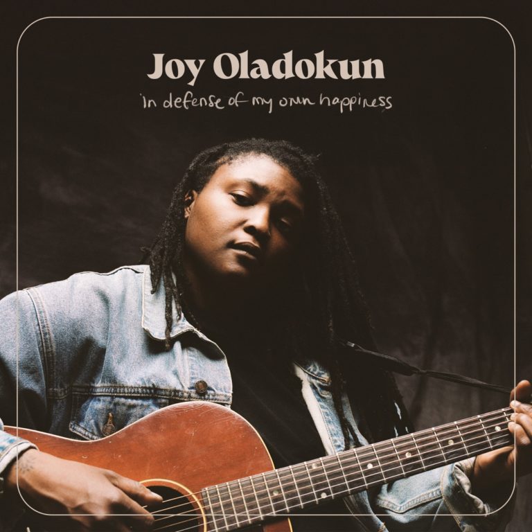 Albumcover von Joy Oladokun – in defense of my own happiness: Joy mit Gitarre im Schoß, Denimjacke, ruhiger Blick, minimalistische Rahmengrafik.