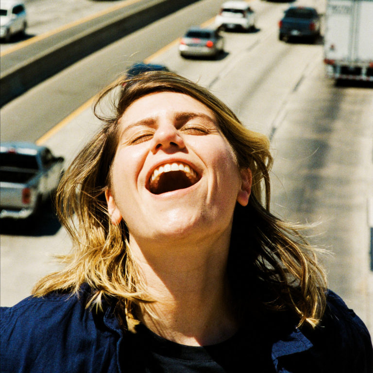 Cover von „The Answer Is Always Yes“ zeigt Alex Lahey lachend auf einer Autobahnbrücke, mit wehenden Haaren und sonniger Energie.
