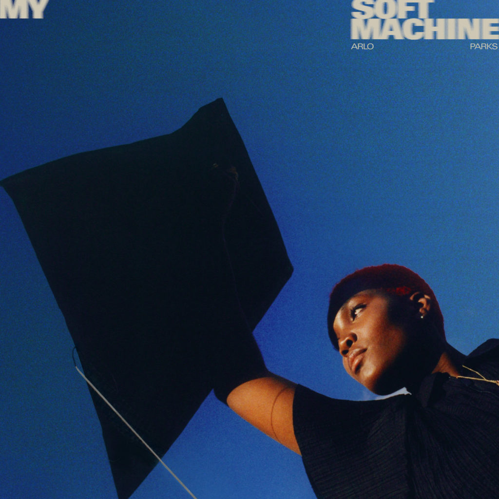 Cover von „My Soft Machine“ zeigt Arlo Parks mit erhobenem Arm vor tiefblauem Himmel – minimalistischer Look mit starker Präsenz.