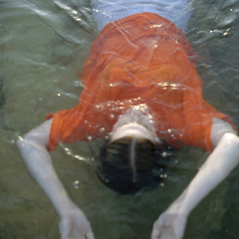 Person in rotem Shirt liegt im Wasser mit ausgestreckten Armen