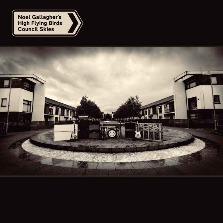 Albumcover von Council Skies von Noel Gallagher’s High Flying Birds: Schwarzweiß-Siedlung mit Instrumenten im Kreisplatz unter dramatischem Himmel.