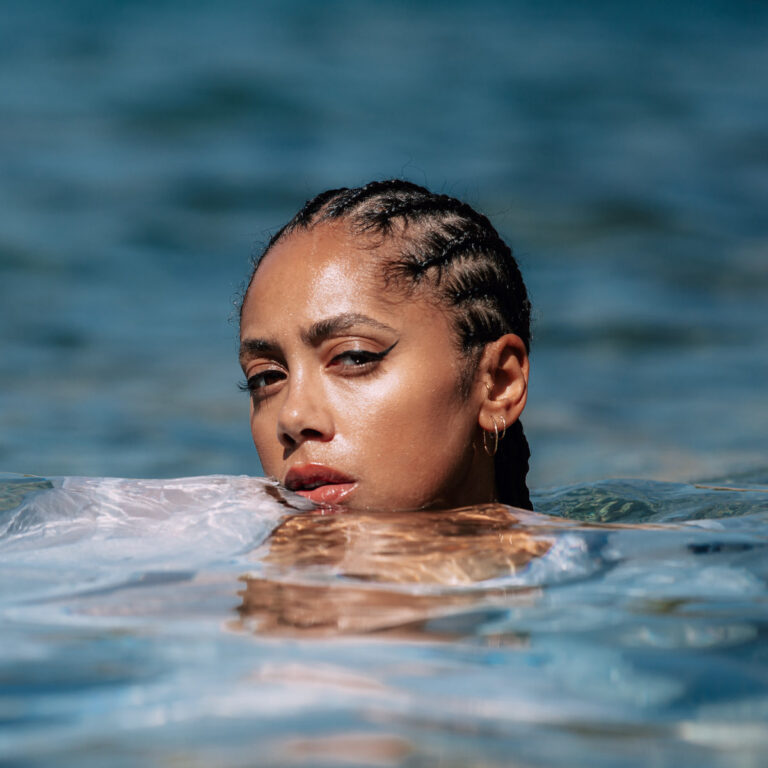 Albumcover zu „Guy“ von Jayda G – Porträt der Künstlerin mit geflochtenem Haar, halb im Wasser, mit nachdenklichem Blick und glitzernder Wasseroberfläche.