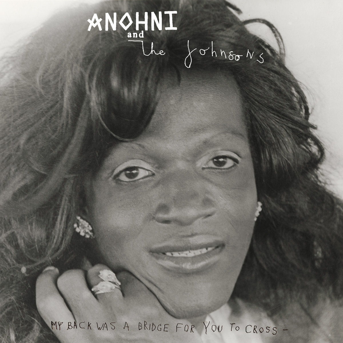 Schwarz-weiß Porträt einer Frau mit glamourösem Styling und warmem Lächeln, Cover des Albums „My Back Was A Bridge For You To Cross“ von ANOHNI and the Johnsons.
