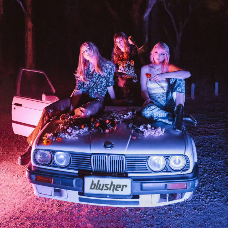Cover der EP „Should We Go Dance?“ von Blusher: Drei Frauen sitzen nachts in buntem Licht auf einem Auto, das mit Blumen geschmückt ist, im Wald.