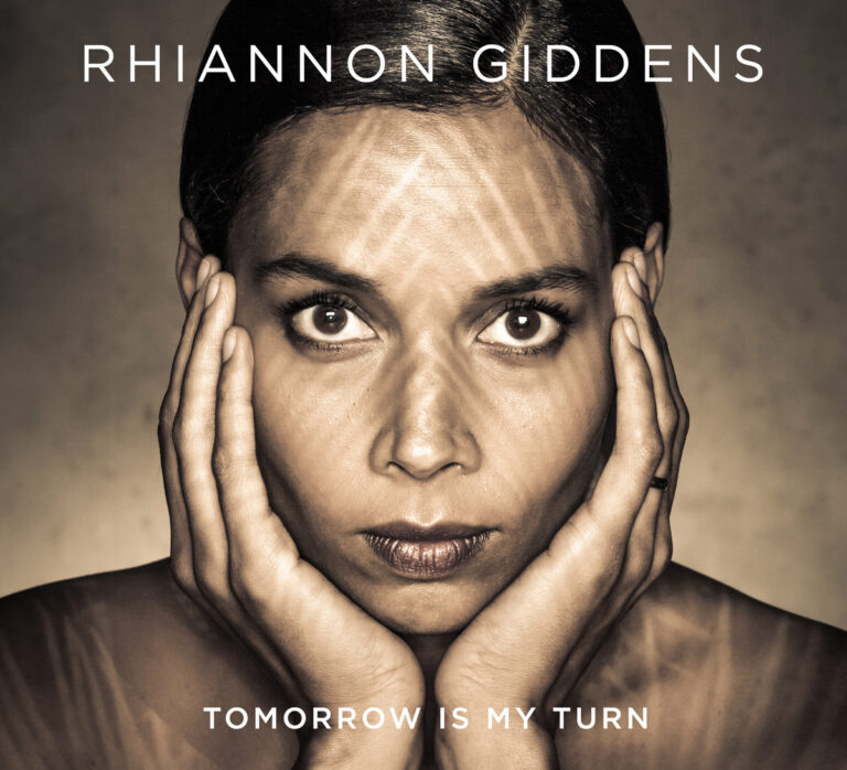 Porträt von Rhiannon Giddens mit nachdenklichem Gesichtsausdruck und Händen an den Wangen.