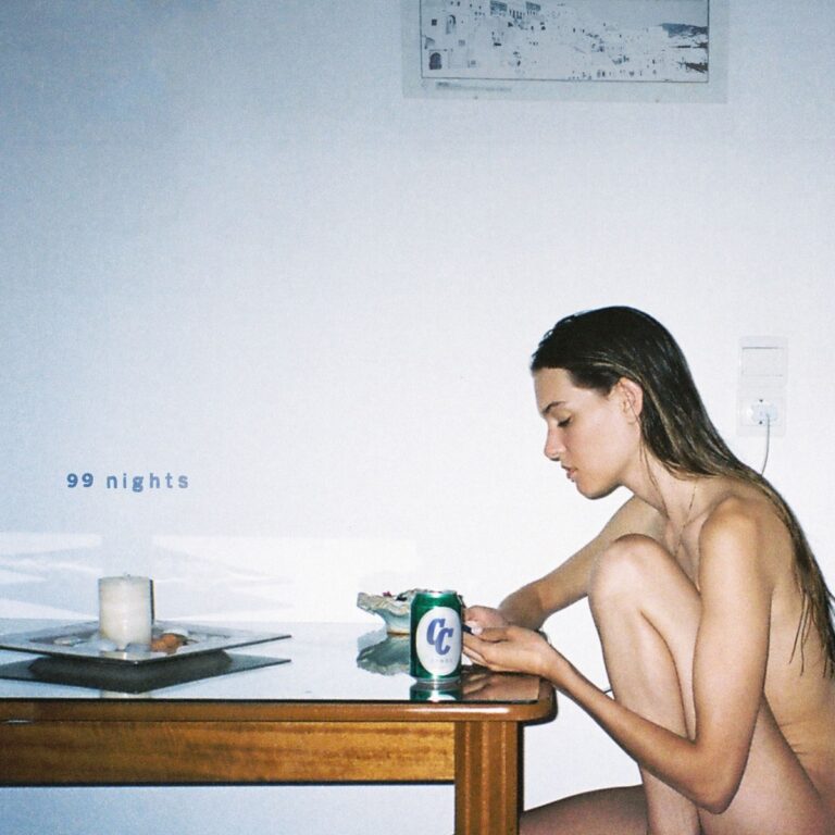 Cover von Charlotte Cardins Album 99 Nights: Eine junge Frau sitzt nackt an einem Tisch, neben ihr eine Dose, Kerze und Snacks, minimalistische Wohnung.