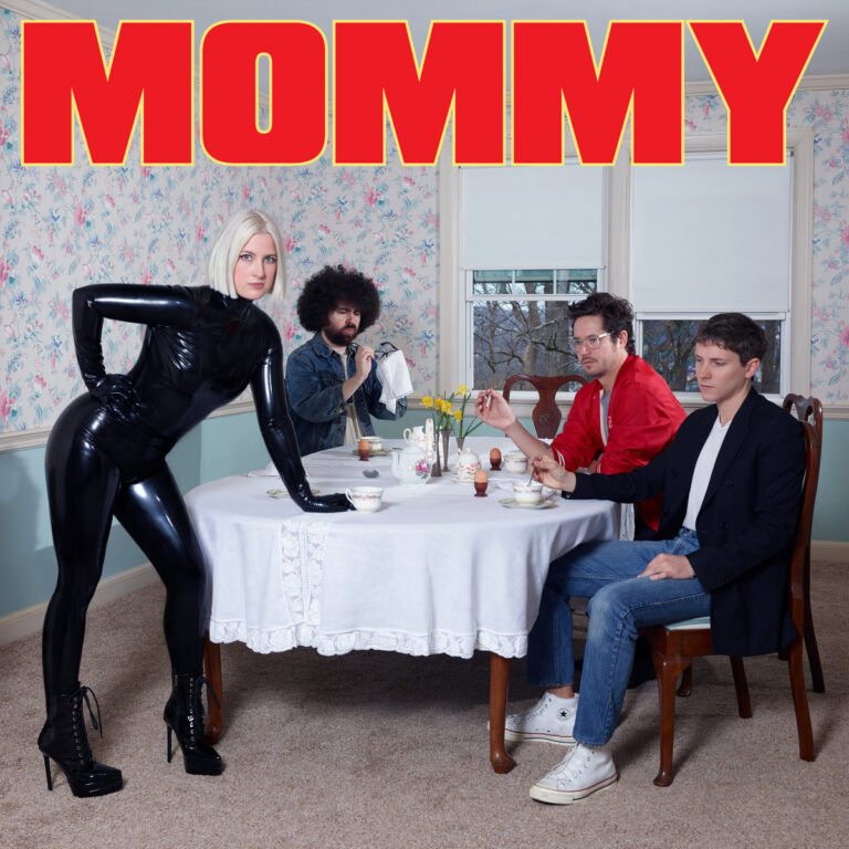 Albumcover von Mommy mit Jemina Pearl im schwarzen Latexanzug vor einem Frühstückstisch mit Bandkollegen, roter Schriftzug „MOMMY“ vor floraler Tapete.
